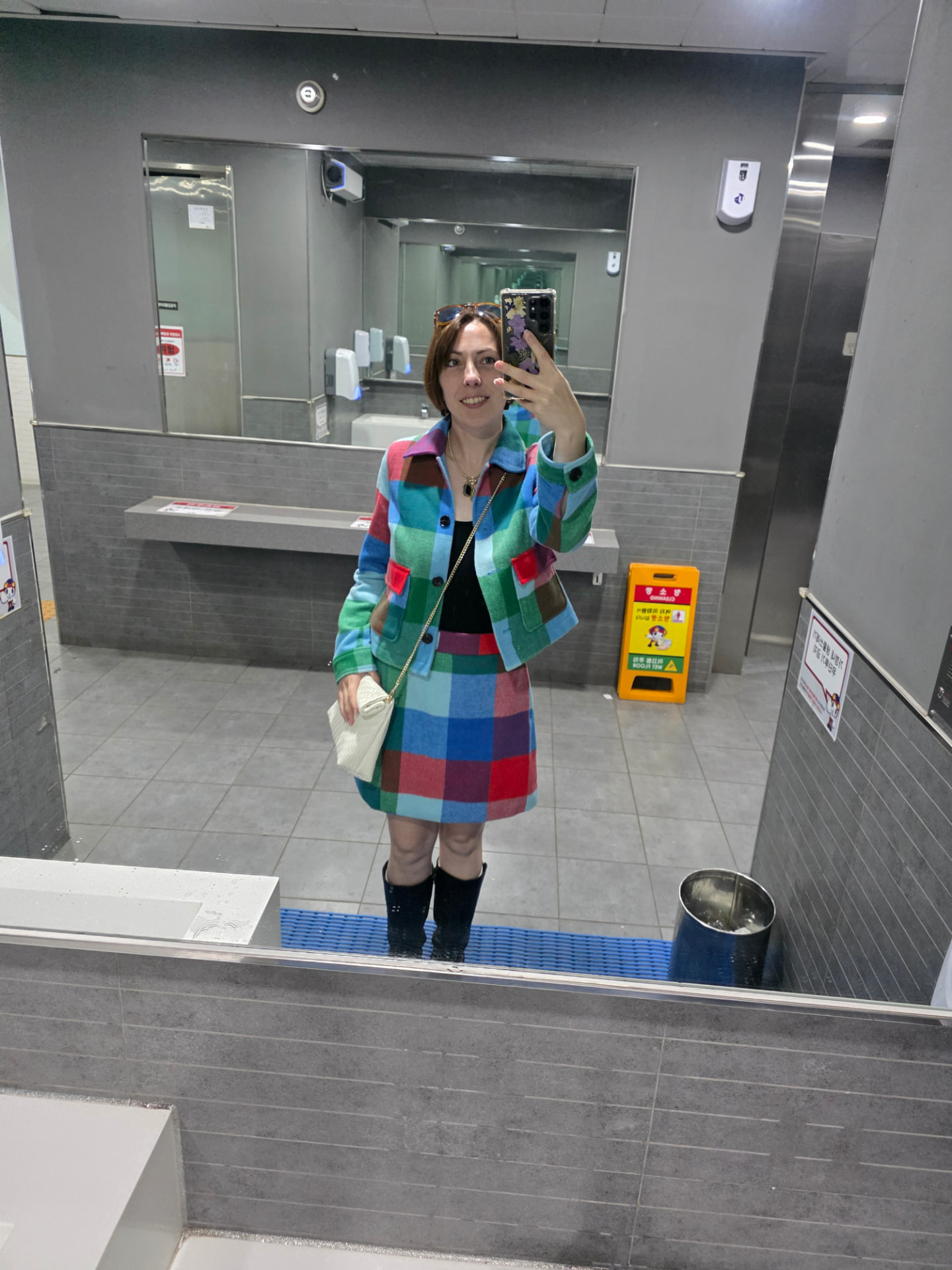 Abi taking a mirror selfie in a colorful checked jacket and skirt with tall black boots